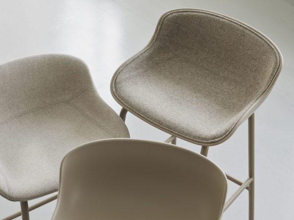 To moderne stole med buet ryg og tekstureret stofbetræk i minimalistisk design med gråt gulv. Den ene stol er beige og den anden er en mørkere sandfarve.