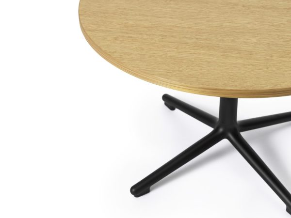 Et nærbillede af et NORMANN COPENHAGEN - Lunar Sofabord Ø70 med en lys træplade og en minimalistisk sort metalbund, placeret mod en skarp hvid baggrund.
