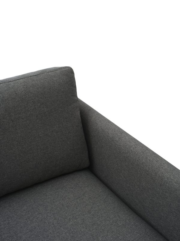 Nærbillede af en mørkegrå sofa med fokus på hjørnet, der viser designmøbler stoftekstur og pudedetaljer mod en hvid baggrund.