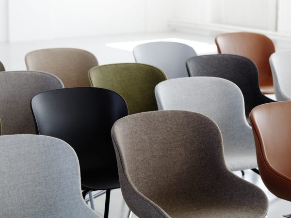 En række moderne stole med forskellige farver og materialer arrangeret i en halvcirkel i et lyst, minimalistisk interiør.