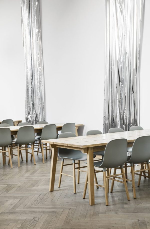 Et moderne spiseområde med rækker af NORMANN COPENHAGEN - Slice Spisebord 90x300 borde med en blanding af hvide og grå stole, sat på baggrund af gulv-til-loft-spejle i krøllet design, over et sildebenstrægulv.