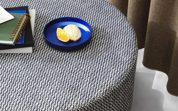 En blå keramisk tallerken med en scone og citronskiver sidder på et gråt tekstureret bord ved siden af en åben notesbog med spiralbinding. Baggrunden viser delvist et draperet brunt stof med TomorrowsDesign.