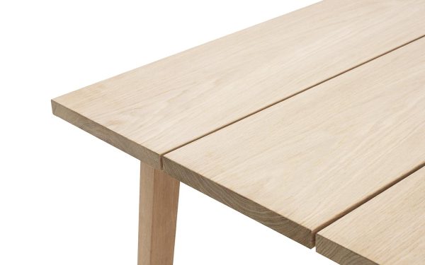 Nærbillede af et NORMANN COPENHAGEN - Slice Spisebord 90x300 hjørne, der viser detaljer af træets årer og snedkerarbejde mod en hvid baggrund.