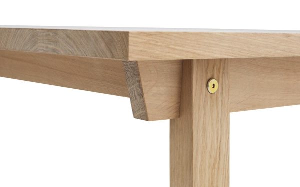 Nærbillede af en NORMANN COPENHAGEN - Slice Spisebord 90x300 med fokus på leddet, hvor bordpladen forbindes med benet, fastgjort med en synlig skrue. Træets årer er tydeligt detaljeret og viser naturlige teksturer og designelementer.