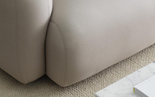 Nærbillede af en NORMANN COPENHAGEN - Swell Sofa 2 Pers. hjørne med tekstureret polstring, delvist overlappende et lignende tekstureret tæppe. et hvidt marmorbord med en notesbog og pen er også synligt.