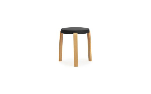 Et moderne NORMANN COPENHAGEN - Tap Skammel med tre lyse træben og et rundt, sort sæde, isoleret på en hvid baggrund.