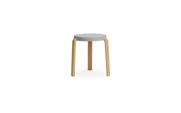 En enkel skammel med et rundt, gråt sæde og tre lyse træben, isoleret på en hvid baggrund. NORMANN COPENHAGEN - Tap Skammel