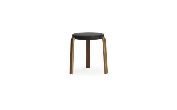 A NORMANN COPENHAGEN - Tap Skammel med en sort rund pude og tre lysebrune træben, stående mod en hvid baggrund.