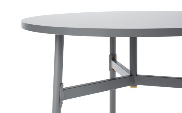 Nærbillede af en NORMANN COPENHAGEN - Union Bord Ø80 med fokus på detaljerne i dens benforbindelser og kanten af bordpladen. Baggrunden er almindelig og hvid.
