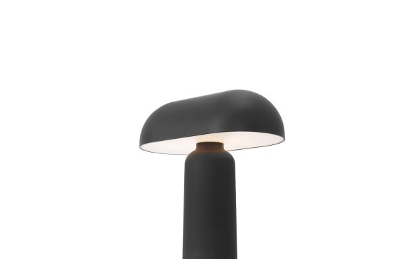 En moderne sort NORMANN COPENHAGEN - Porta Bordlampe med en cylindrisk base og en glat, kuppelformet top, der udsender et blødt, nedadrettet lys, sat mod en almindelig hvid baggrund.