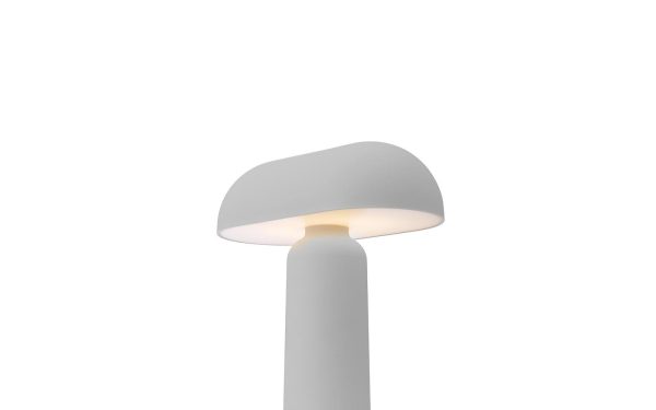 En moderne bordlampe med en mat grå finish har en kuppelformet skærm på et cylindrisk stativ, der udsender et varmt, blødt lys. Designet er minimalistisk og slankt, sat mod en almindelig hvid baggrund, perfekt til moderne interiør-æstetik.