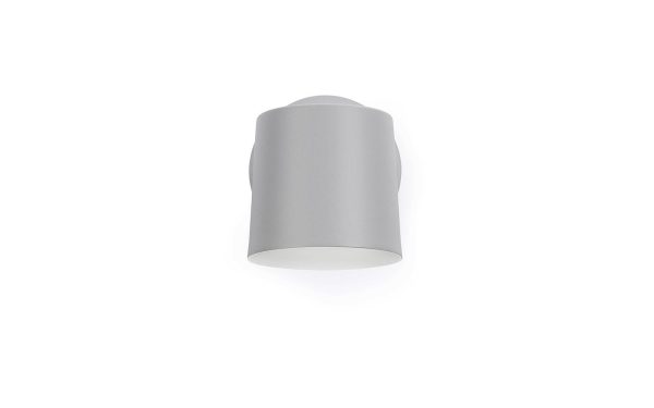 En moderne, cylindrisk NORMANN COPENHAGEN - Rise Væglampe monteret på en almindelig hvid baggrund, der udsender et blødt skær fra bunden.