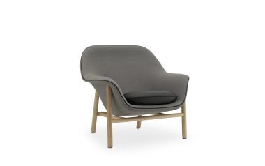 En moderne lænestol med et gråt stofbetræk og træben, isoleret på en hvid baggrund. NORMANN COPENHAGEN - Drape Loungestol har en behagelig pude og et slankt, moderne design.