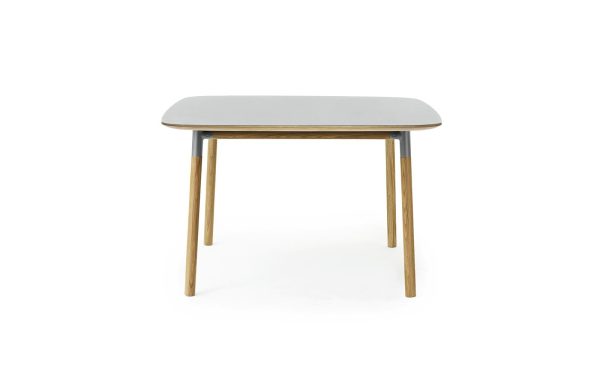 Et moderne bord med en rektangulær, grå bordplade og fire træben, isoleret på en hvid baggrund. Designet er enkelt og moderne.