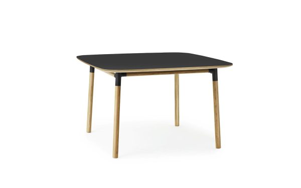 Et moderne firkantet bord med sort bordplade og lyse træben, der viser moderne design, isoleret på en hvid baggrund.