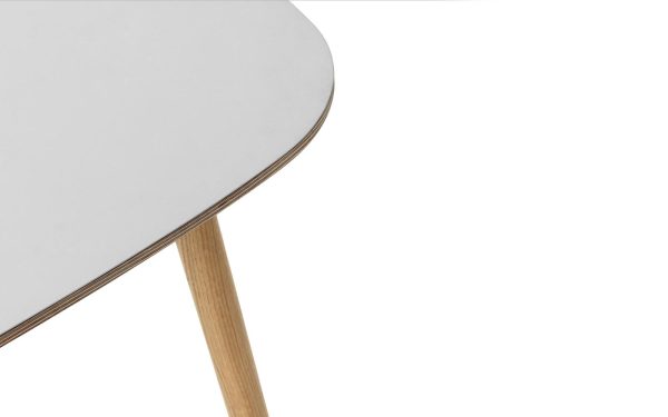 Delvis visning af et moderne bord med en slank, rund hvid plade og et enkelt synligt træben, sat mod en almindelig hvid baggrund. Dette stykke eksemplificerer moderne interiørdesign.