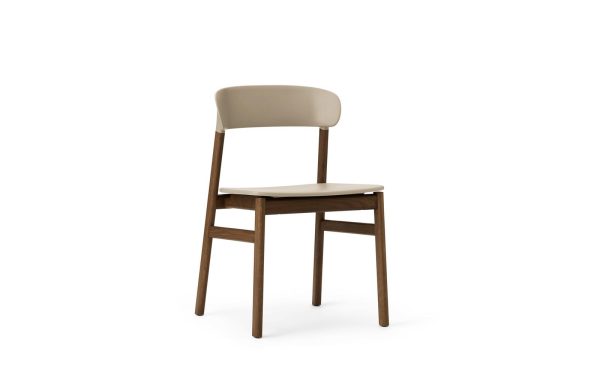 En moderne stol med beige polstret ryglæn og sæde, og mørkebrune træben, isoleret på en hvid baggrund.(Produktnavn: NORMANN COPENHAGEN - Herit Spisebordsstol)