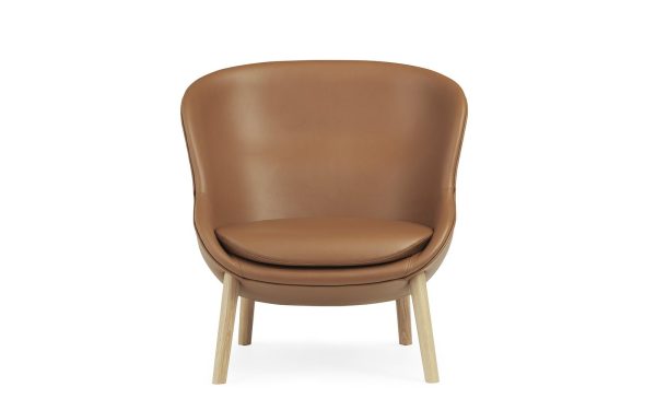 En moderne stol med glat, NORMANN COPENHAGEN - Hyg Lænestol Lavt polstring og træben, isoleret på hvid baggrund.