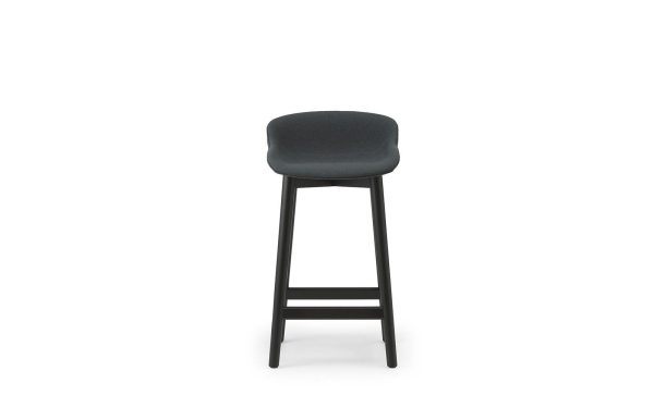 En moderne NORMANN COPENHAGEN - Hyg Barstol 65 med et polstret sæde og ryglæn på høje sorte ben, placeret foran en almindelig hvid baggrund.