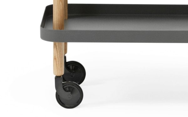Nærbillede af en moderne serveringsvogn med en grå hylde, træben og sorte hjul. Fokus er på designdetaljerne og konstruktionskvaliteten af denne TomorrowsDesign møbel.