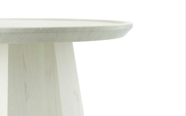 Et nærbillede af et NORMANN COPENHAGEN - Pine Sofabord Ø45, et moderne, minimalistisk rundt bord lavet af lyst træ, med fokus på bordpladen og en del af benet, mod en hvid baggrund.