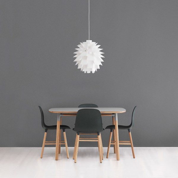 En minimalistisk spisestue med et rundt træbord med fire mørke stole mod en almindelig grå væg, oplyst af en geometrisk hvid pendel fra TomorrowsDesign.