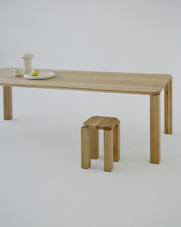 Et minimalistisk træbord og skammel sat mod en almindelig baggrund. Bordet, et stykke TomorrowsDesign-håndværk, er udstyret med en lille tallerken, en kop og en lysestage.