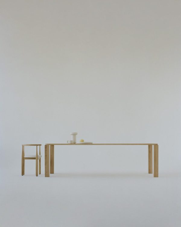 Et minimalistisk interiør med et træbord og en stol mod en almindelig, lys baggrund. På bordet er der et par simple hvide og pastelfarvede keramiske genstande. Dette rum afspejler gennemtænkte designmøbler-principper.