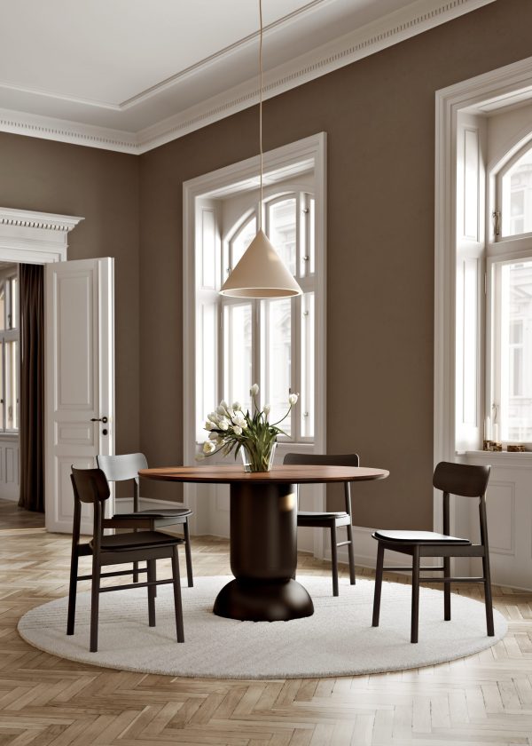 En sofistikeret spisestue med et rundt bord med en sort sokkel, omgivet af tre stole. En pendel hænger ovenover. Rummet har højt til loftet, detaljerede lister og store vinduer. Den kan prale af udsøgte designmøbler, der forstærker dens elegance.