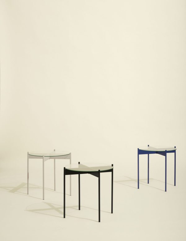 Tre minimalistiske borde i forskellige højder og farver, med glasoverflader med skygger støbt på en lys baggrund. Scenen er præget af enkelhed og elegance i møbeldesign.