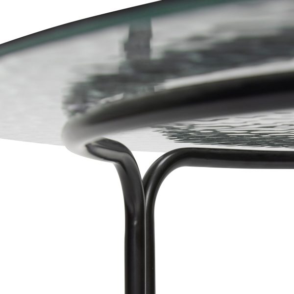 Nærbillede af et moderne glasbord med sort metalstel, med TomorrowsDesign-mærket, hvor glaspladen møder stellet, alt sammen mod en hvid baggrund.