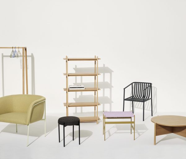 En moderne stueopstilling med en grøn sofa, sort metalstol, træhylde, lille sort skammel, pink polstret bænk og et rundt sofabord i træ på en almindelig baggrund af TomorrowsDesign.