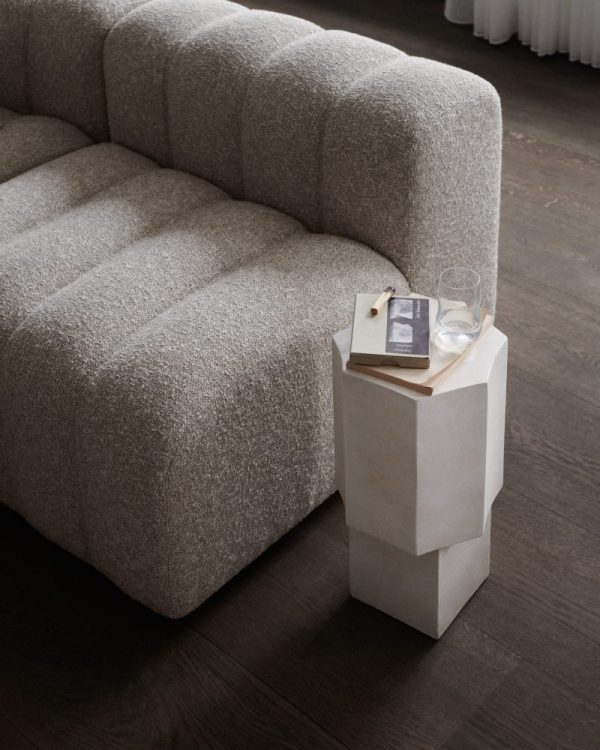 Et minimalistisk stuehjørne med en tekstureret grå sofa med en NORR11 - Quartz Sidebord med en bog, et glas vand og en lille dekorativ genstand, sat på et mørkt trægulv.
