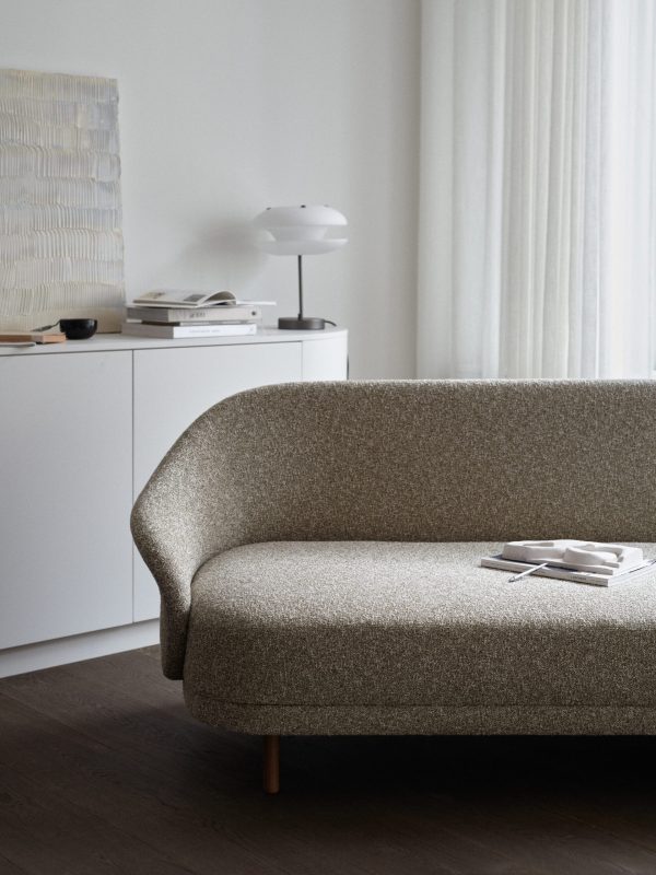Moderne stuehjørne med en tekstureret solbrun sofa, en hvid skænk med en NORR11 - Yo-Yo Bordlampe og en bog sat op mod hvide vægge og gennemsigtige gardiner.
