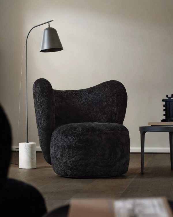 En mørk tekstureret lænestol og matchende skammel i et minimalistisk rum med en NORR11 - Line One Gulvlampe, en lille hvid vase og et lavt bord med bøger. Blødt, naturligt lys oplyser scenen.