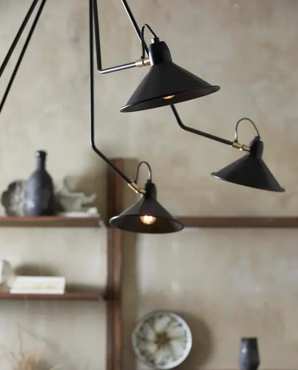 Tre sorte pendellamper med en metallisk finish, der hænger over en rustik træhylde med forskellige dekorative genstande fra TomorrowsDesign, mod en struktureret beige væg.