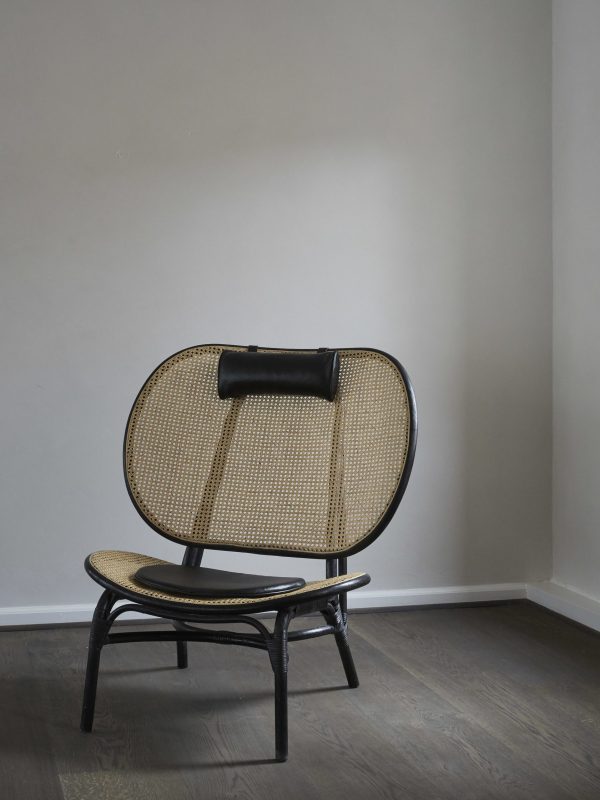 En moderne sort stol med afrundet ryg og vævet sæde, sat mod en almindelig grå væg på et trægulv. Stolen har en sort hynde på den øverste del af ryglænet og eksemplificerer TomorrowsDesign-æstetik.