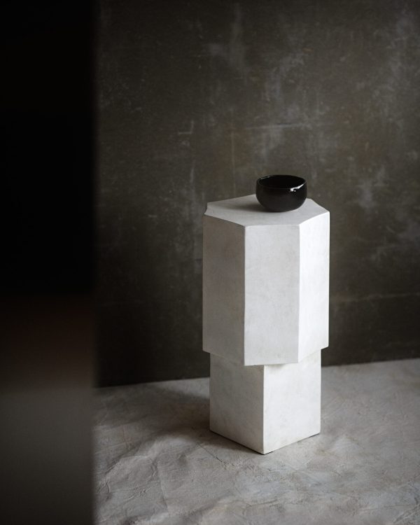 En lille, sort skål sidder oven på en NORR11 - Quartz Sidebord i et rum med grå vægge og et matchende gulv, der fremkalder en minimalistisk og fredfyldt stemning.
