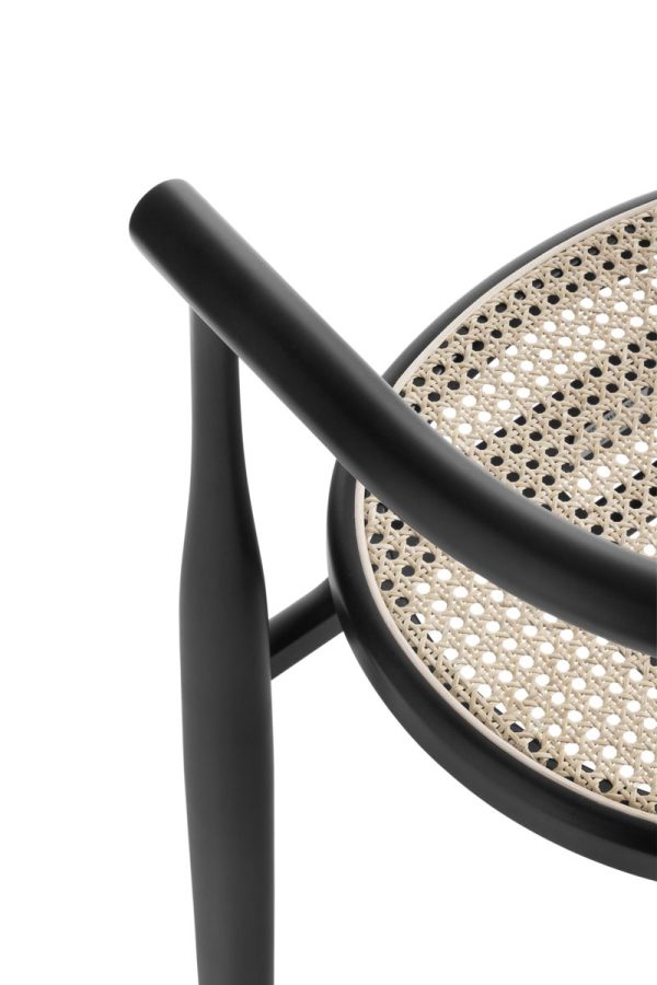 Nærbillede af en moderne stol med sort stel og et vævet stoksæde, der viser det slanke design og detaljerne i armlænet og sædemønsteret. Baggrunden er almindelig hvid. Dette stykke er indbegrebet af TomorrowsDesign i alle aspekter af dets interiør-æstetik.