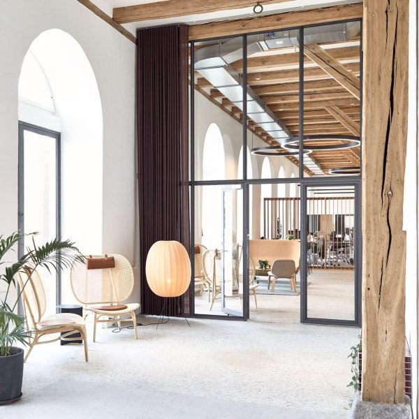 Moderne kontorlobby med store glasdøre, buede hvide vinduer og træmøbler, herunder en rattanstol og en unik kugleformet lampe.