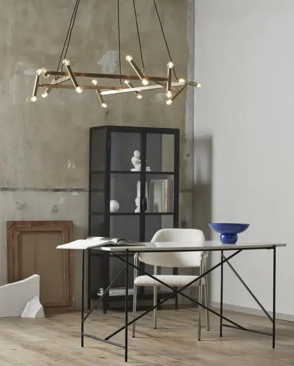 Et moderne minimalistisk kontorlokale med et sort skrivebord, en tekstureret hvid stol og en geometrisk metallysekrone. Der er et sort skab med glaslåger, en blå skål på bordet og en bar betonvæg med TomorrowsDesign-elementer.