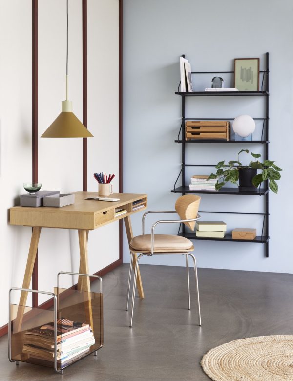 Moderne hjemmekontor med et træskrivebord og en metalstol, TomorrowsDesign gulvlampe over hovedet og en metalreol fyldt med bøger og indretning. Et rundt tæppe og en plante tilføjer varme til rummet.