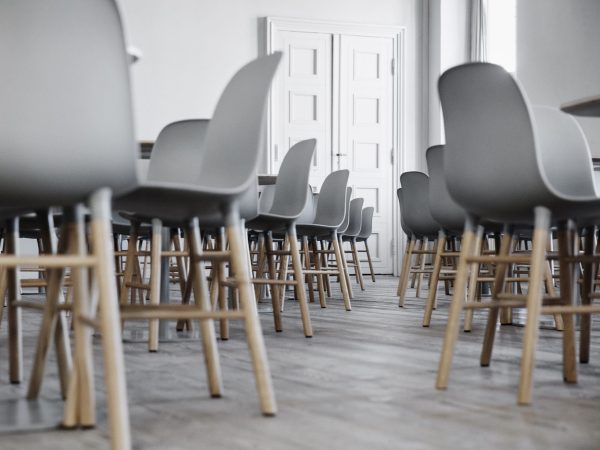 Et moderne mødelokale med rækker af grå stole sat på træben, designet til at vende mod et sæt lukkede hvide dobbeltdøre for enden af lokalet. Gulvet er af træ og væggene er hvidmalede.