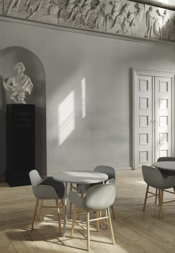 En minimalistisk moderne spisestue med et rundt bord med grå stole, sat i et klassisk rum med udsmykkede skulpturelle detaljer, en statue i en niche og lys, der strømmer gennem et vindue. Dette rum viser udsøgte designmøbler, der komplementerer det overordnede interiør.