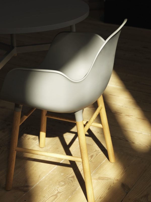 En moderne grå stol med træben står under naturligt sollys og kaster skarpe skygger på et trægulv. Dette stykke viser enestående interiørdesign.