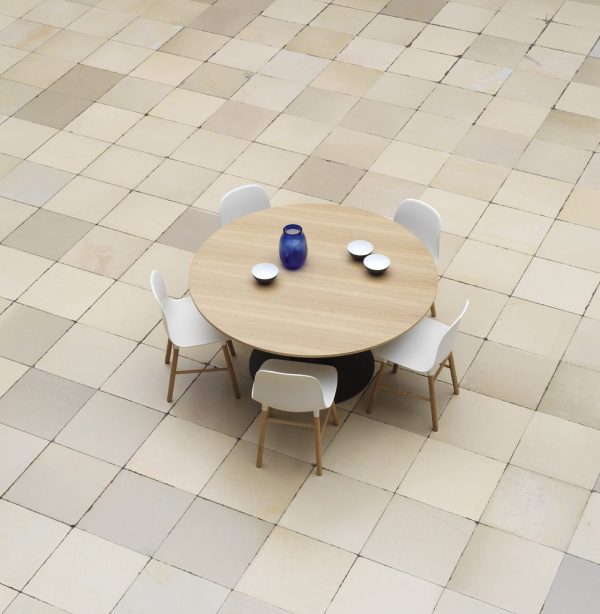 Et rundt træbord med fire hvide stole på et beige klinkegulv, sat med en blå vase og tre hvide tallerkener, der viser TomorrowsDesign-æstetik.