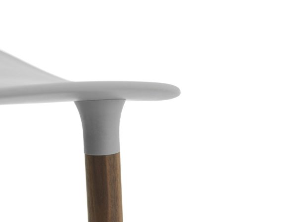 Nærbillede af en NORMANN COPENHAGEN - Form Barstol 65's detaljer, der viser samlingen mellem dets glatte, hvide sæde og det ene træben mod en almindelig, lys baggrund.