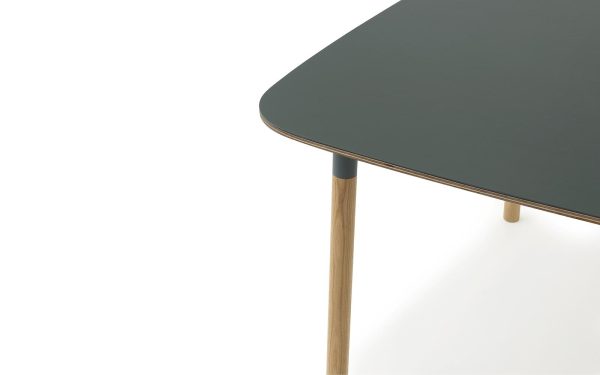 Nærbillede af et moderne bord med en mørkegrå plade og træben med metalaccenter, sat mod en hvid baggrund. Designet er minimalistisk og slankt, hvilket afspejler moderne designprincipper.