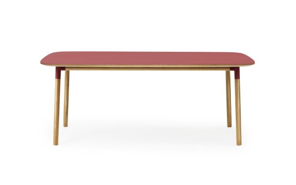 Et moderne, aflangt bord med rød bordplade og fire vinklede lyse træben fra TomorrowsDesign, isoleret på hvid baggrund.