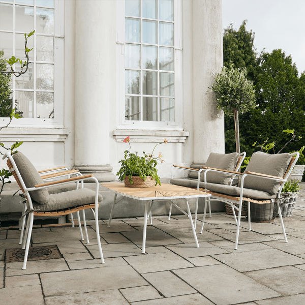 Et udendørs siddeområde med to moderne loungestole med hynder og et lille bord, sat på en stenterrasse ved siden af en klassisk hvid søjlebygning med store vinduer og grønne planter, designet af TomorrowsDesign.